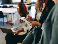 Three employees taking notes: one has a computer, the other has a pen and paper.